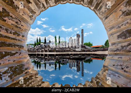 Ruins of the sanctuary of Apollon Smintheus and its reflection in the puddle through the carved out marble column in Ayvacik, Turkey. Stock Photo