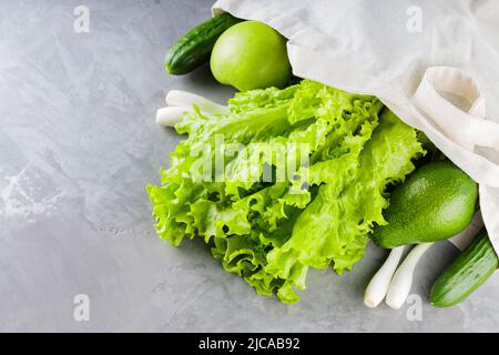 Green vegetables and fruits, greenery in shopping cotton bag. Eco linen bag with green fruits and vegetables on a gray background. Reasonable consumpt Stock Photo