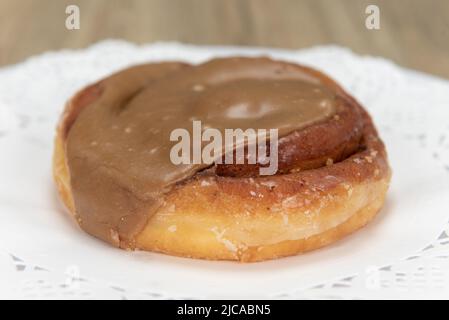 Tempting fresh from the oven cinnamon roll maple donut from the bakery served on a plate. Stock Photo