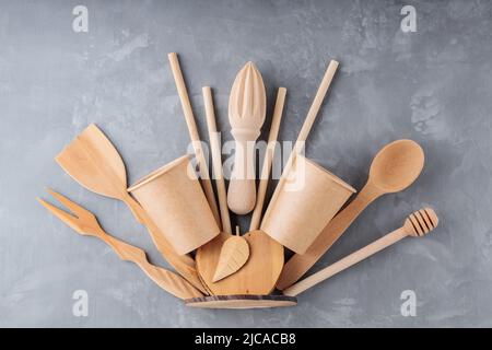 Reusable wooden kitchen utensils on gray background. Wooden kitchenware, bamboo straw and disposable paper cups on concrete. Sustainable lifestyle. Pl Stock Photo