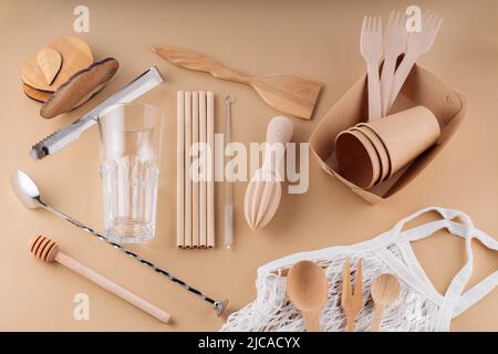 Wooden cutlery, paper disposable tableware and bar tools on a beige background. Eco-friendly kitchen utensils and mesh bag. Zero waste, plastic free c Stock Photo