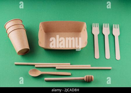 Eco-friendly tableware, paper disposable cup and wooden cutlery on a green background. Environmentally friendly disposable tableware, bamboo straws an Stock Photo