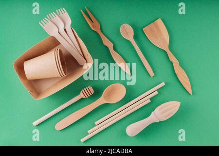 Eco-friendly tableware, paper disposable cup and wooden cutlery on a green background. Environmentally friendly disposable tableware, bamboo straws an Stock Photo