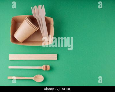 Eco-friendly tableware, paper disposable cup and wooden cutlery on a green background. Environmentally friendly disposable tableware, bamboo straws an Stock Photo