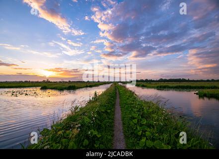 Path over a dike in Holland under colorful skies during sunset Stock Photo