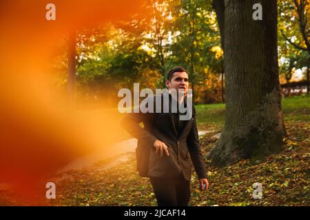 Portrait young man on nature autumn background. Serious young man. 20s years. Handsome man outdoors portrait. Orange colored. Walking in park. Pocket. Stock Photo