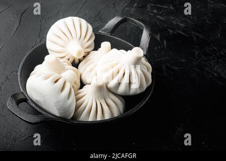 Frozen Raw dumplings Khinkali with beef and lamb meat, in frying cast iron pan, on black stone background, with copy space for text Stock Photo