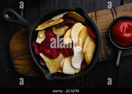 Dried vegetables chips from carrot, beet, parsnip and other vegetables, on black wooden table background, top view flat lay Stock Photo