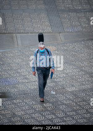 Medellin, Antioquia, Colombia - March 6 2022: An Old Man with White Hair Wears a Cyan Mask, Carries a Guitar on his Back and Walks Down the Street on Stock Photo