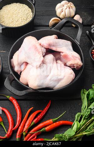 Raw chicken wings with herbs, and sesame, in frying cast iron pan, on black wooden table Stock Photo