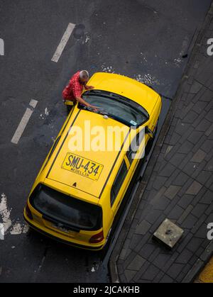Medellin, Antioquia, Colombia - March 6 2022: Cab Driver Cleaning his Yellow Car Parked on Street Corner Stock Photo