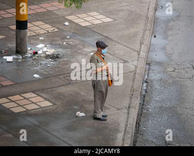 Medellin, Antioquia, Colombia - March 6 2022: An Elderly Man Wears a Black Cap and Cyan Mask, Carries a Bag Slung Over his Shoulder and Wants to Cross Stock Photo