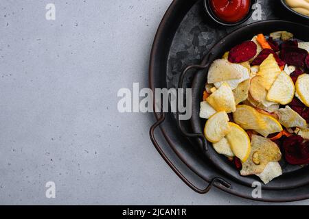 Dried vegetables chips from carrot, beet, parsnip and other vegetables, on gray stone table background, top view flat lay, with copy space for text Stock Photo