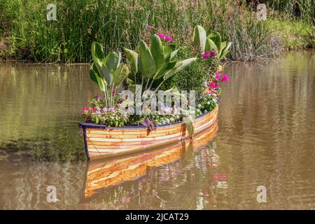 Vintage rowboat filled with flowers and tropical plants floating on pond with reflection in water. Stock Photo