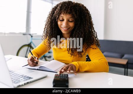 Smiling african american woman working with computer and calculator at home Stock Photo