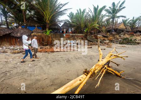 Two people walk by the beach erosion from the storm the went by. Driftwood and other debris are all around. Stock Photo