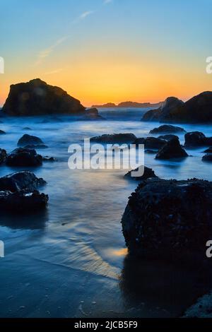 Smooth waves around rocks on beach at golden hour in California Stock Photo