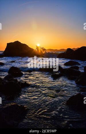 Sun sets on beach with waves and rocks Stock Photo