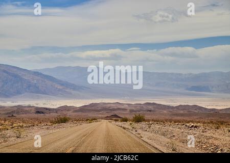 Open desert road in Death Valley leading to large mountains and sandy plains Stock Photo