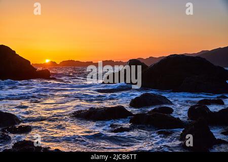 Sunset golden hour on beach covered in ocean waves and rocks Stock Photo
