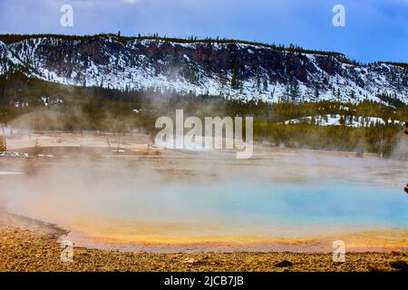 Sulfuric steam hovers over beautiful spring in Yellowstone snowy mountains Stock Photo