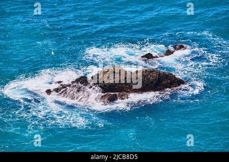 Large rocks in ocean water with waves crashing into them Stock Photo