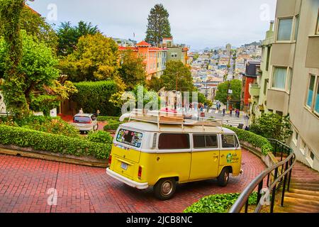 Red brick road curving down with yellow and white Volkswagen bus Stock Photo