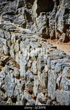 Stone wall next to rocky cliffs and hiking path Stock Photo