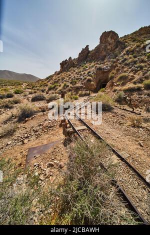 Tracks leading into mountainside with mine entrance in desert Stock Photo