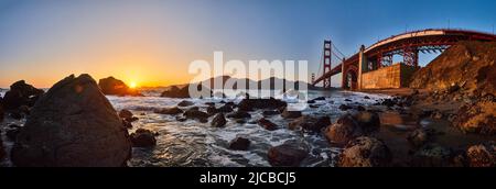 Stunning panorama of Golden Gate Bridge on ocean coast with rocks and sunset Stock Photo