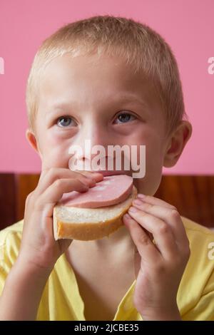 boy eats bread with boiled sausage in the room Stock Photo