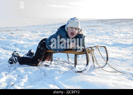 Winter fun - sledding at winter time. Young boy enjoying a sledge ride in a snowy winter park. Stock Photo