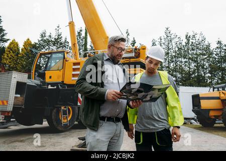 Foreman and customer or client agree about future building work on construction site. architect discussing project with builder over crane vehicle Stock Photo