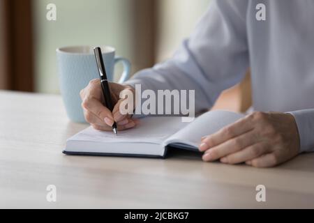 Close up cropped older woman writing notes in paper planner Stock Photo