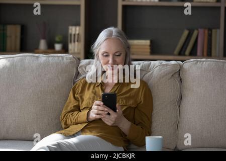 Beautiful middle-aged woman spend leisure at home using smartphone Stock Photo