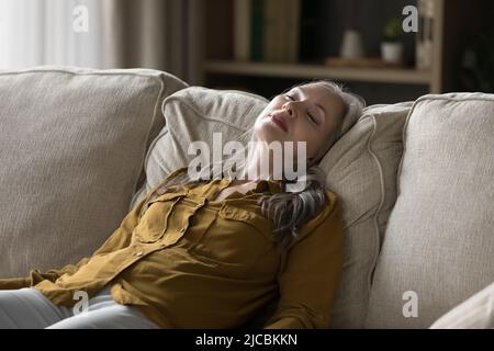 Peaceful middle aged woman sleeping leaned on sofa Stock Photo