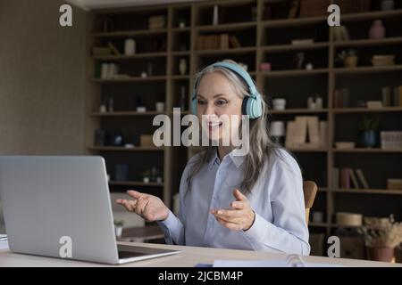 Older woman in headphones using laptop make video conference Stock Photo