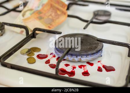 blood coming out of a gas lit gas burner next to ukrainian currency, Hrivni. War victims metaphor Stock Photo