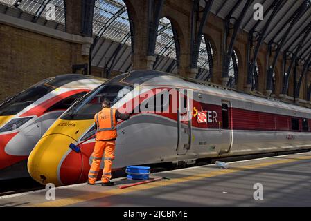 A member of railway staff cleans an LNER Azuma High Speed train At Kings Cross Station, London, UK Stock Photo