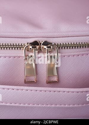 gold zippers with gold zippers are fastened on a pink leather object, close-up Stock Photo