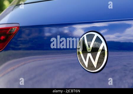 A chrome VW emblem logo is seen on the rear of a new, blue Volkswagen Golf. Stock Photo