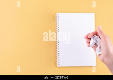 the hand crumpling the page of the notebook on a yellow background. space for text. turning over a new leaf Stock Photo