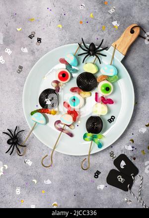 Top view of plate with colorful jelly, eyeballs, candy, marshmallows on skewers. Stock Photo