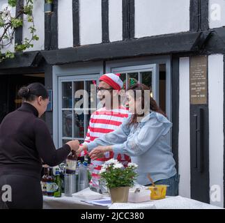 Man in red & white striped fancy dress & woman serve beer outside Friends Restaurant during St George’s Day Celebration 2022, Pinner, Harrow, London. Stock Photo