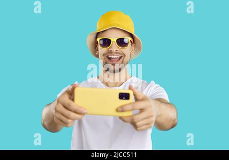 Cheerful carefree guy making selfie shot on mobile phone on light blue background. Stock Photo