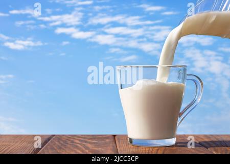 milk pouring from jug into glass cup on table Stock Photo