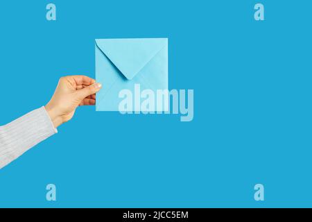 Human hand holding blue paper envelope with letter or message on blue background Stock Photo