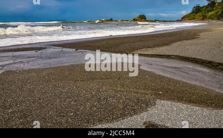 A small river that flows into the Pacific Ocean erodes the sandy shore in Olympic National Park, Washington Stock Photo