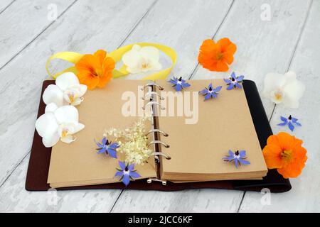 Leather bound journal or diary with blank pages for personal notes or story, with orchid flowers, nasturtium and borage herb flowers. On rustic wood. Stock Photo