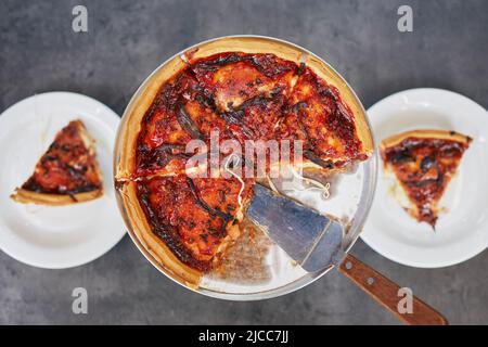 Deep dish pizza with tomato sauce for two person on table in restaurant. Stock Photo